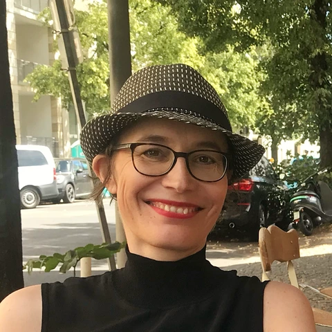 Sabine, stellvertretende Vorsitzende von Leben nach Krebs! e.V. — Porträt mit Hut und Brille, lächelnd in einem Café